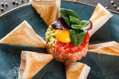 Biftek tartare bir yumurta sarısı, doğranmış avokado, domates ve tost karanlık taş zemin üzerine plaka ile devam eder. Yeme sağlıklı gıda kavramı temiz