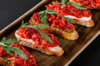 Meze bruschetta ciabatta ekmeği ve sosu pesto plaka siyah taş zemin üzerine doğranmış sebze ile. Vejetaryen yiyecekler kavramı. Lezzetli aperatifler, crostini, piknik zamanında kanepe