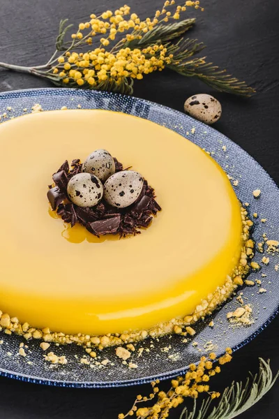 Bolo de Páscoa com esmalte espelho amarelo, chocolate, flores da primavera, ovos de codorna no fundo de pedra escura. Feliz celebração da Páscoa . — Fotografia de Stock