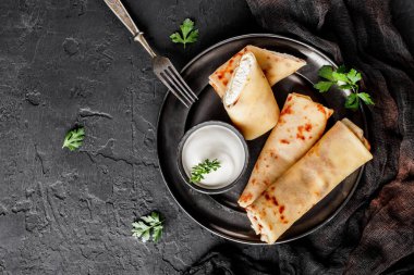 Krep peynir, yeşil ve koyu arka plan üzerinde siyah plaka üzerinde ekşi krema ile. Krep hafta ya da Shrovetide. Sağlıklı kahvaltı. Üstten Görünüm, düz yatıyordu