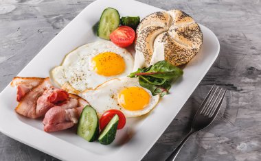 Kahvaltı, sahanda yumurta, topuz, pastırma, salam, plaka gri masa yüzeyi üzerinde taze salata. Sağlıklı gıda, üstten görünüm, düz yatıyordu.