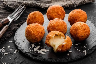 Fried potato cheese balls or croquettes with spices on black plate over dark stone background. Unhealthy food. clipart