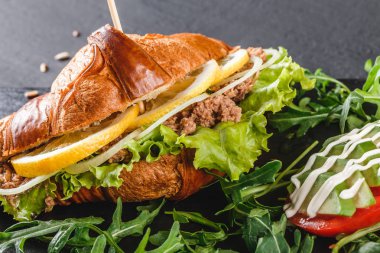 Ton balığı, avokado, taze roka ve Yeşiller siyah taş zemin üzerine siyah şeyl gemide sandviç. Sağlıklı gıda kavramı