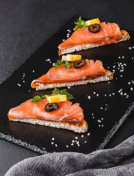 Förrätt bruschetta med filé lax, oliver och citron på ciabatta bröd på stone skiffer bakgrund. Hälsosam matkoncept. — Stockfoto