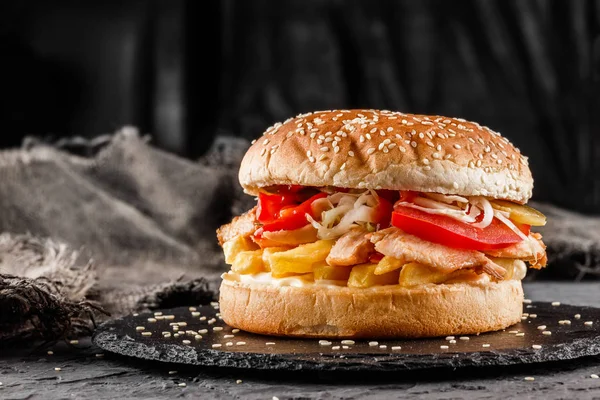 Chicken burger with tomatoes, french fries and sauce on black slate over dark background. Unhealthy food — Stock Photo, Image