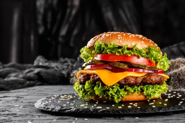 Говяжий бургер с сыром, помидорами, красным луком, огурцом и салатом на черном фоне. Нездоровая пища — стоковое фото
