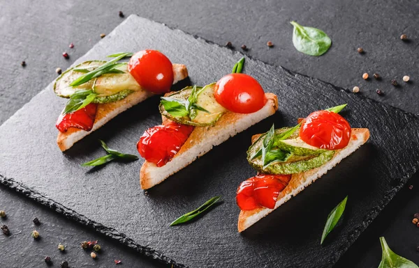 Aperitivo bruschetta con verduras, tomates y especias en pizarra de esquisto negro sobre fondo de piedra negra. Concepto de comida saludable . — Foto de Stock