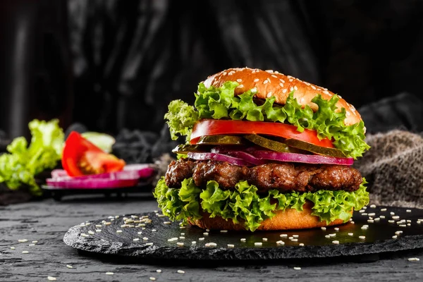 Говяжий бургер с помидорами, красным луком, огурцом и салатом на черном фоне. Нездоровая пища . — стоковое фото
