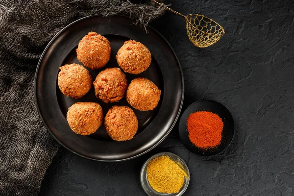 Bolas de queso de patata frita o croquetas con especias en plato negro sobre fondo de piedra oscura. Comida poco saludable, vista superior . —  Fotos de Stock