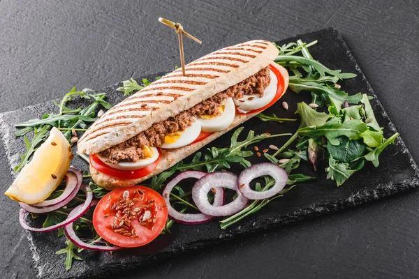 Sandwich con atún, huevos, verduras frescas y verduras en pizarra de esquisto negro sobre fondo de piedra negra. Concepto de comida saludable . — Foto de Stock