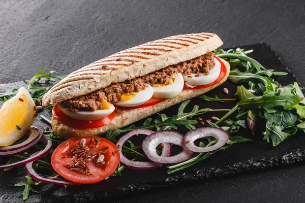 Sandwich con atún, huevos, verduras frescas y verduras en pizarra de esquisto negro sobre fondo de piedra negra. Concepto de comida saludable . — Foto de Stock