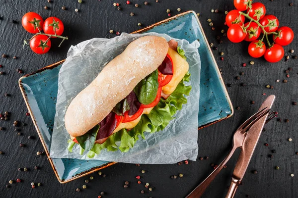 Sandwiches frescos con jamón, queso, tocino, tomates, lechuga en plato sobre fondo de piedra oscura. Almuerzo saludable . — Foto de Stock