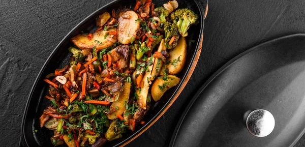 Запечені овочі, зелень, картопля, броколі в сковороді на фоні чорного каменю. Чисте харчування, здорове вегетаріанське харчування. Вид зверху, плоский ліжко — стокове фото
