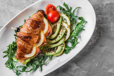 Kırmızı balıklı kruvasan sandviçi, avokado, taze sebzeler ve siyah taş zemin üzerinde roka. Sağlıklı gıda konsepti