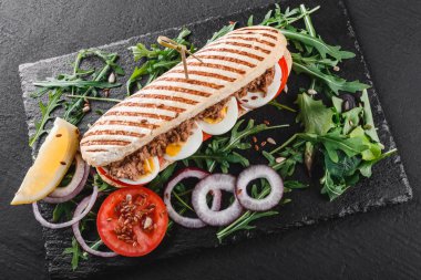 Ton balığı, yumurta, taze sebze ve Yeşiller siyah taş zemin üzerine siyah şeyl gemide ile sandviç. Sağlıklı gıda kavramı. Üstten görünüm, düz yatıyordu