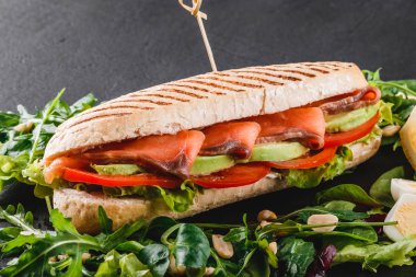 Sandviç kırmızı balık, yumurta, avokado, taze sebze ve Yeşiller siyah taş zemin üzerine siyah şeyl gemide. Sağlıklı gıda kavramı