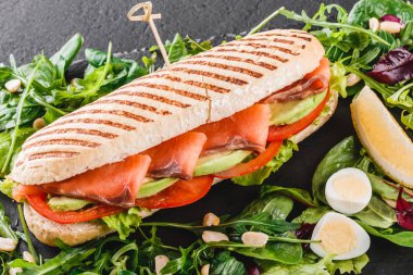 Sandviç kırmızı balık, yumurta, avokado, taze sebze ve Yeşiller siyah taş zemin üzerine siyah şeyl gemide. Sağlıklı gıda kavramı