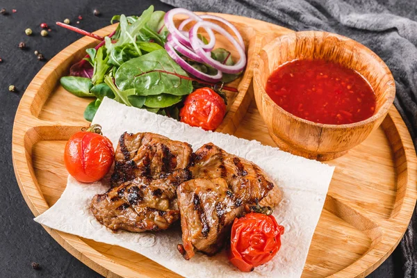 Мясо на гриле свинины и овощи со свежим салатом и соусом барбекю на разделочной доске на черном каменном фоне. Горячее мясо . — стоковое фото