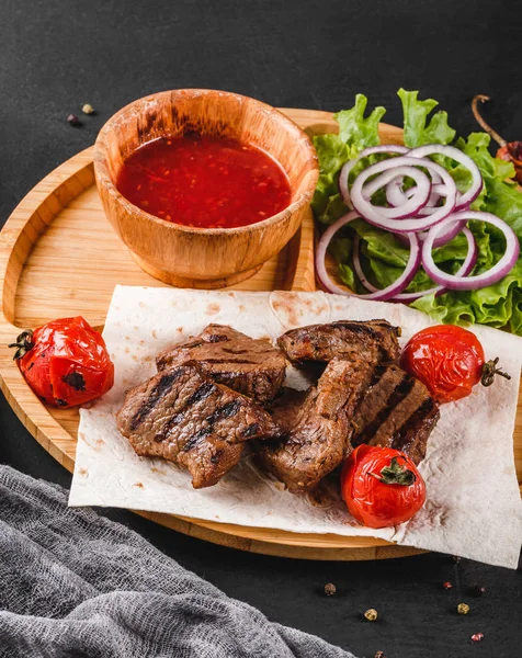 Grillowane mięso wołowe i warzywa ze świeżą sałatką i sosem BBQ na deski do krojenia na czarnym tle kamienia. Gorące dania mięsne. — Zdjęcie stockowe