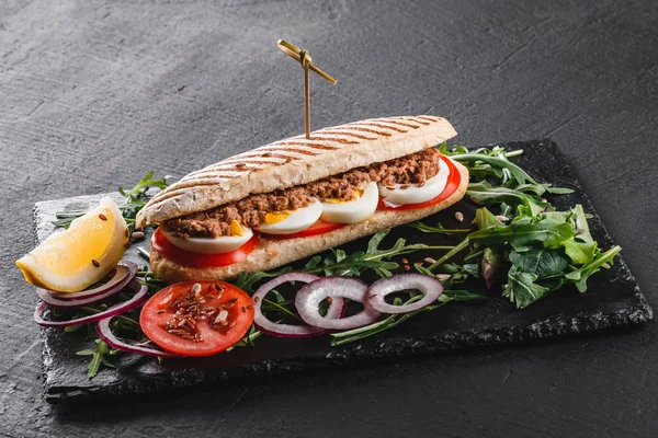 Sandwich con atún, huevos, verduras frescas y verduras en pizarra de esquisto negro sobre fondo de piedra negra. Concepto de comida saludable . — Foto de Stock