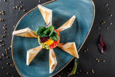 Biftek tartare bir yumurta sarısı, doğranmış avokado, domates ve tost karanlık taş zemin üzerine plaka ile devam eder. Yeme sağlıklı gıda kavramı temiz