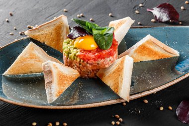 Biftek tartare bir yumurta sarısı, doğranmış avokado, domates ve tost karanlık taş zemin üzerine plaka ile devam eder. Yeme sağlıklı gıda kavramı temiz