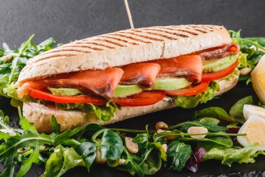 Sandviç kırmızı balık, yumurta, avokado, taze sebze ve Yeşiller siyah taş zemin üzerine siyah şeyl gemide. Sağlıklı gıda kavramı