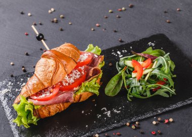 Sandviç ile jambon, domates, peynir parmesan ve siyah şeyl gemide yeşillik siyah taş arka plan üzerinde. Sağlıklı gıda kavramı