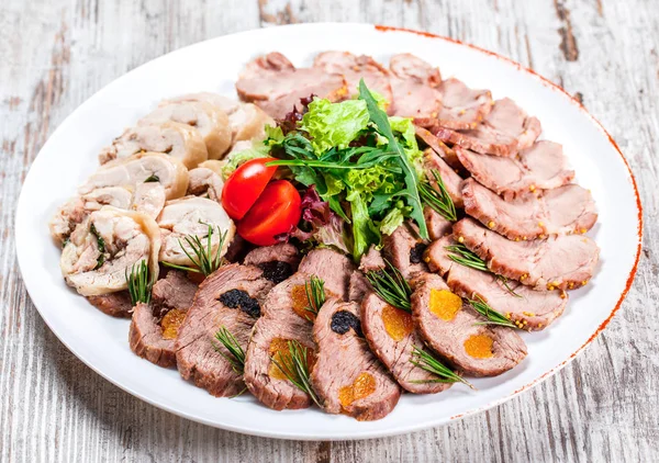 Assorted meat appetizer, cow\'s tongue, ham, stuffed chicken roll, meat roll with pepper, greens on plate over rustic background. Meat appetizer, food concept