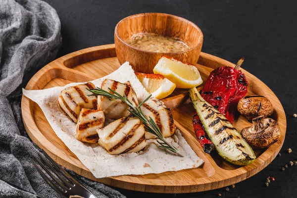 Izgara fileto balık ve sebze kesme tahtası üzerinde siyah taş zemin üzerine baharat soslu. Sıcak balık yemekleri.