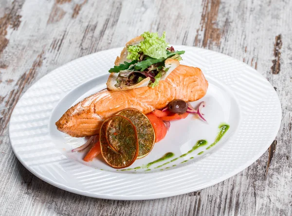 Запеченный лосось, украшенный оливками, зеленью, помидорами на деревянном фоне. Горячая рыба . — стоковое фото