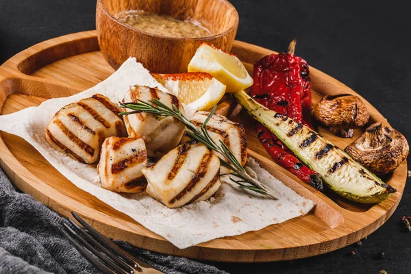 Izgara fileto balık ve sebze kesme tahtası üzerinde siyah taş zemin üzerine baharat soslu. Sıcak balık yemekleri.