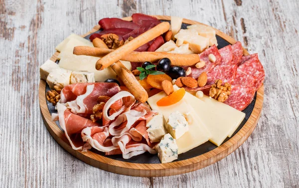 Antipasto platter cold meat with grissini bread sticks, prosciutto, slices ham, beef jerky, salami and cheese platter on wooden board over rustic background. Appetizer, catering food concept