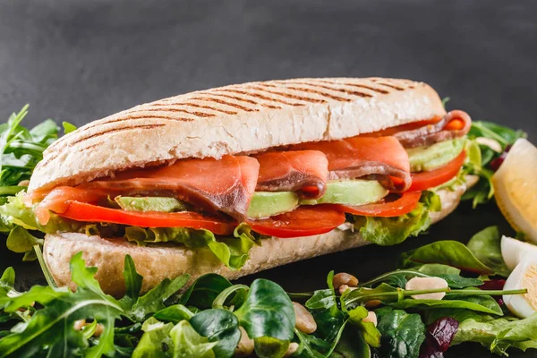 Sandviç kırmızı balık, yumurta, avokado, taze sebze ve Yeşiller siyah taş zemin üzerine siyah şeyl gemide. Sağlıklı gıda kavramı