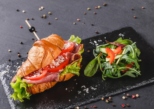 Sandwich con jamón, tomates, queso parmesano y verduras en pizarra de esquisto negro sobre fondo de piedra negra. Concepto de comida saludable — Foto de Stock