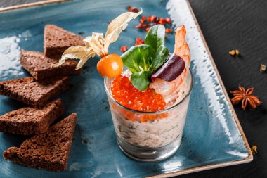 Karides ve kırmızı havyar physalis ve Yeşiller plaka üzerinde süslenmiş siyah arka plan üzerinde siyah ekmek ile snack. Sağlıklı gıda