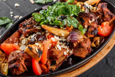 Siyah taş arka planda tava ızgara sebzeler, yeşillikler ve badem ile pişmiş et. Sıcak et yemekleri.