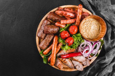 Çeşitli lezzetli ızgara et ve sosis domates ve kesme tahtası siyah taş zemin üzerine Barbekü sosu ile. Sıcak et yemekleri. Üstten görünüm, düz yatıyordu
