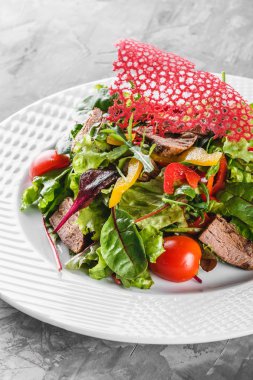 Marul, roka, tatlı biber, domates ve plaka üzerinde karanlık tablo içinde sığır eti taze yeşil salata. Sağlıklı gıda, diyet.