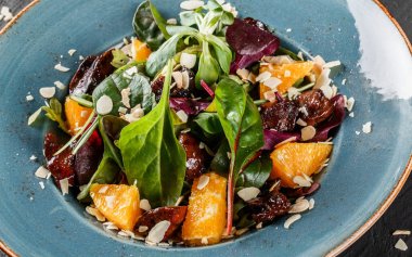 Koyu taş yüzey üzerinde plaka üzerinde karaciğer, Arugula, turuncu, ıspanak ve badem ile salata. Sağlıklı gıda konsepti. Üst görünüm.