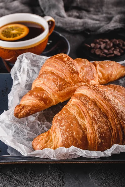 Reggeli friss francia csokis croissant a papíron több mint sötét háttér szalvétára és csésze teát. Desszert, puff Pastries, felülnézet — Stock Fotó