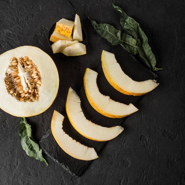 Yellow melon on black stone background. Colorful fresh fruit. Top view, flat lay, copy space.