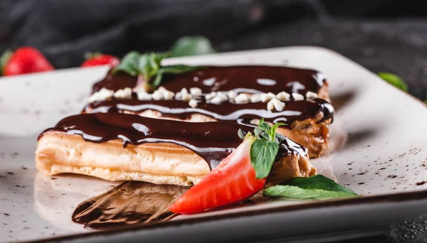 Hemlagad kaka eclairs eller bakelser med vaniljsås, choklad och jordgubbar på mörk bakgrund serveras med kopp kaffe. Traditionella franska eclairs, dessert. Närbild — Stockfoto