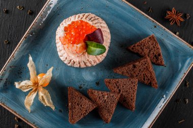 Karides ve kırmızı havyar physalis ve Yeşiller plaka üzerinde süslenmiş siyah arka plan üzerinde siyah ekmek ile snack. Sağlıklı gıda