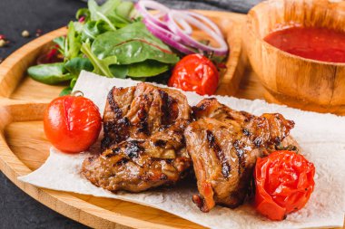 Siyah taş arka planda kesme tahtasında taze salata ve barbekü sosu ile ızgara domuz eti ve sebzeler. Sıcak et yemekleri.