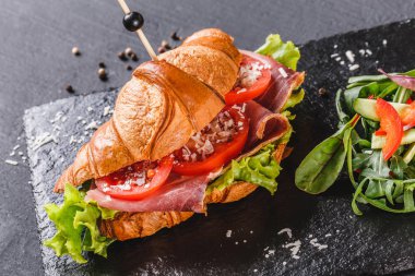 Prosciutto, domates, peynirli parmesan peynirli kruvasan sandviçi ve siyah taş arka planda siyah şist tahtası. Sağlıklı gıda konsepti