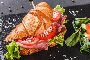 Prosciutto, domates, peynirli parmesan peynirli kruvasan sandviçi ve siyah taş arka planda siyah şist tahtası. Sağlıklı gıda konsepti