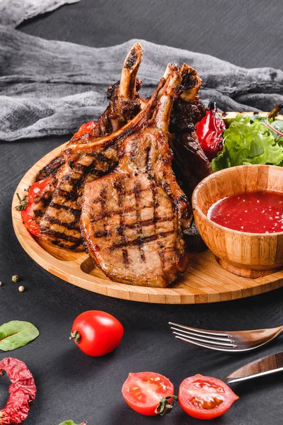 Grillowany stek z grilla na kości i warzywa ze świeżą sałatką i sosem BBQ na płycie do cięcia na czarnym tle kamienia. Gorące dania mięsne — Zdjęcie stockowe