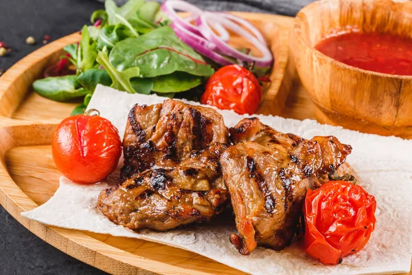 Siyah taş arka planda kesme tahtasında taze salata ve barbekü sosu ile ızgara domuz eti ve sebzeler. Sıcak et yemekleri.