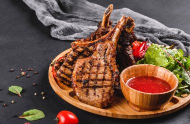 Siyah taş arka planda kesme tahtasında taze salata ve barbekü sosu ile kemik ve sebzeler üzerinde ızgara ribeye Steak. Sıcak et yemekleri.